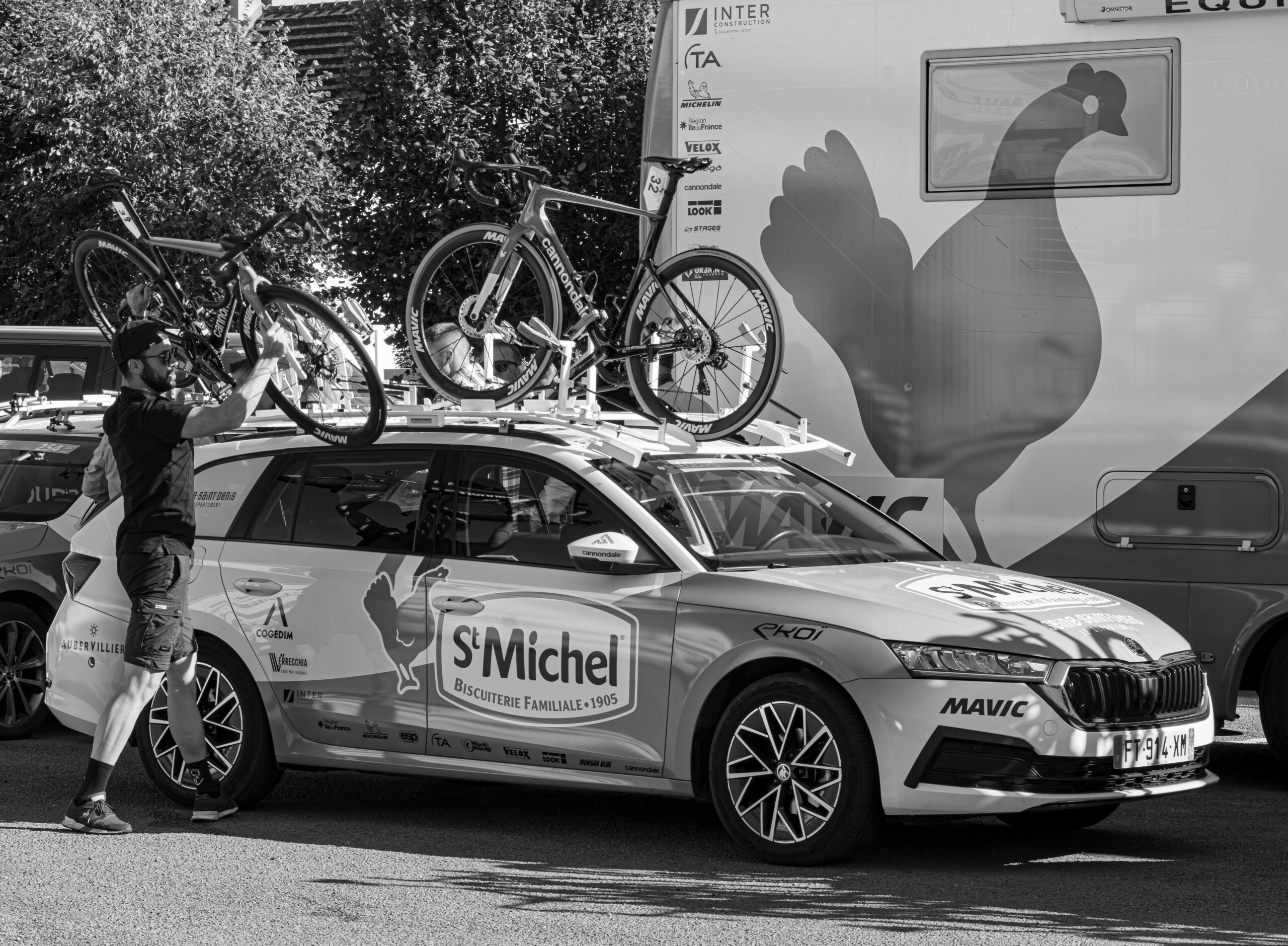 Man securing bicycles on a Skoda support vehicle in an urban setting, perfect for sports event coverage.